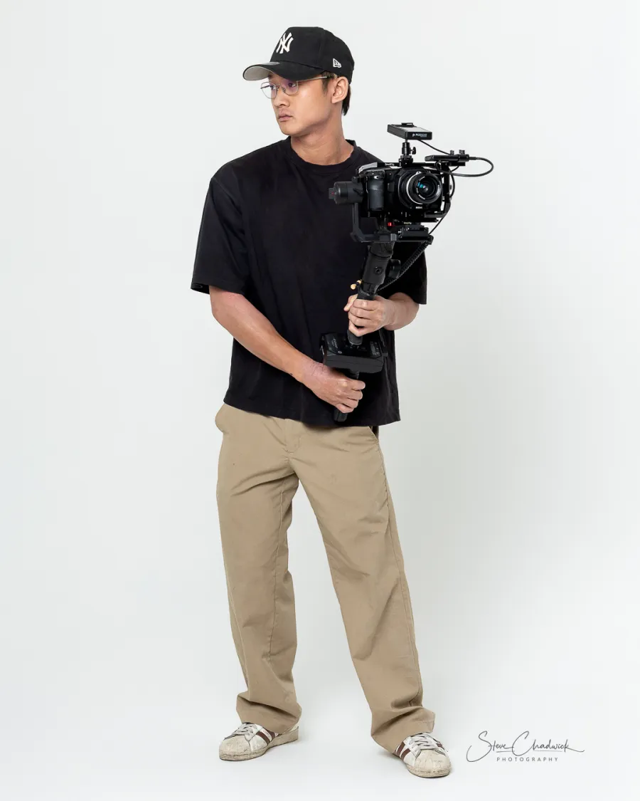 Filmmaker holding a gimbal-mounted cinema camera, full-length studio portrait